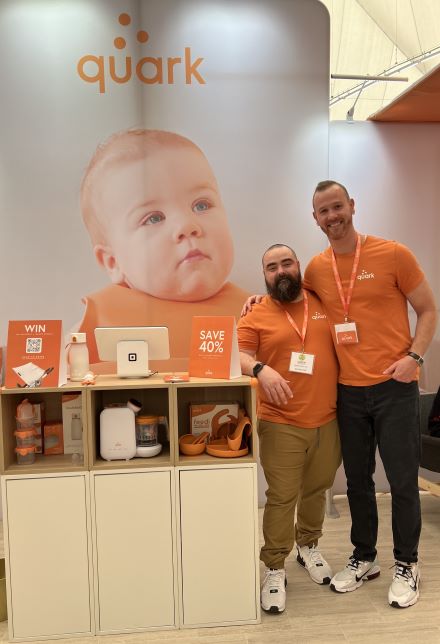 誇克聯合創始人塞內茲（Senez）和古林斯卡斯（Gurinskas）站在貿易展臺的產品旁邊。 背面有他們的標誌的嬰兒照片。